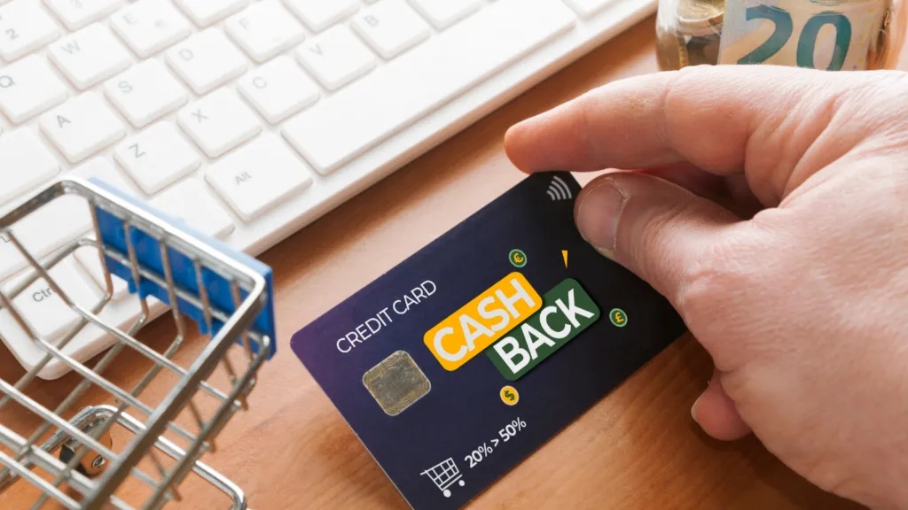 A person holding a cashback card in their hands next to a keyboard, supermarket basket and a jar of money.