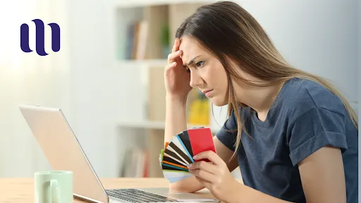 woman-looks-worried-at-the-laptop-screen-while-holding-several-cards-in-her-hand