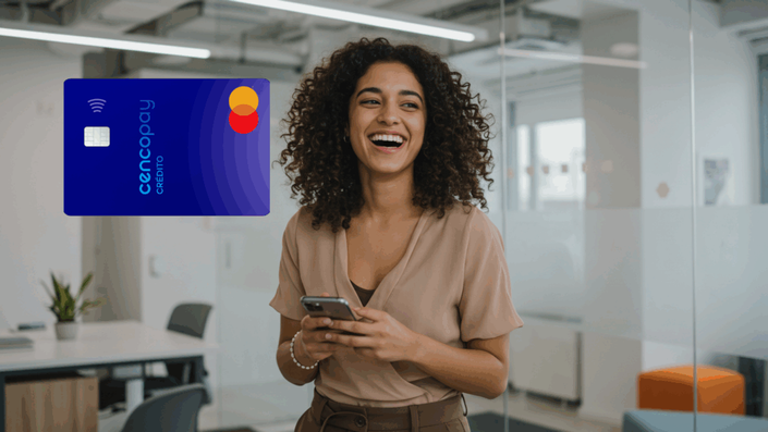 Mujer joven de cabello rizado sonriendo mientras sostiene un celular en una oficina acristalada. A la izquierda, se visualiza una tarjeta de crédito Cencopay Mastercard de diseño azul con logo contactless.