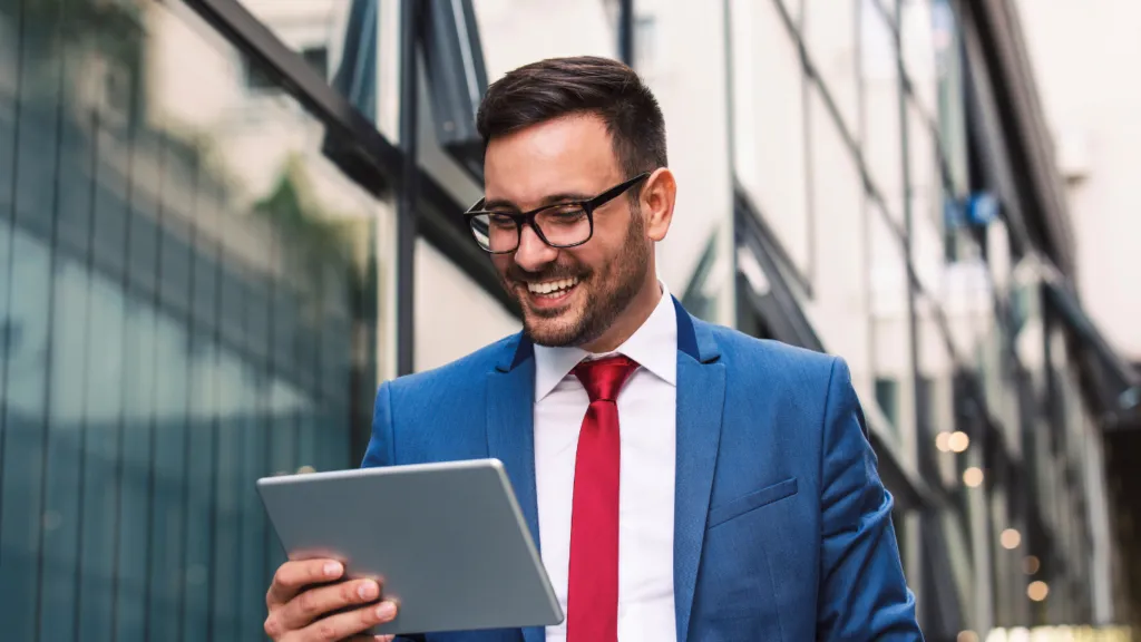 A man in glasses and a suit viewing a tablet and smiling