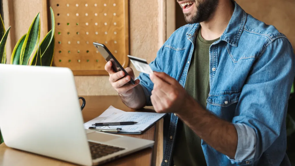 Man with a credit card in his hands looking at his cell phone