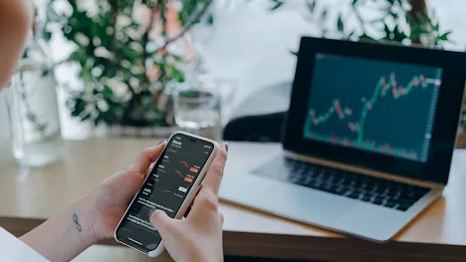 a person investing and analyzing charts on their computer and cell phone