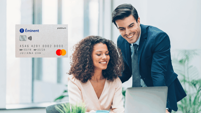 Dos profesionales sonrientes revisando información en una laptop en un entorno de oficina moderno. A la izquierda, se muestra una tarjeta de crédito Mastercard Platinum de Éminent.