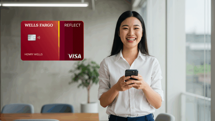 Mujer sonriente usando su teléfono móvil mientras sostiene una tarjeta de crédito Wells Fargo Reflect Visa. La imagen transmite un ambiente moderno y profesional.