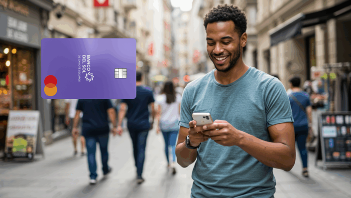 Hombre joven sonriente en una calle comercial, usando su celular. A la izquierda, se visualiza una tarjeta de crédito morada del Banco del Sol con el logo de Mastercard.