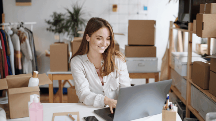 Emprendedora sonriente gestionando su tienda online de dropshipping en Argentina desde su laptop, rodeada de cajas y productos, demostrando la operatividad del negocio.