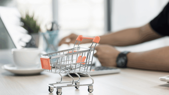 Miniatura de carrito de compras sobre un escritorio, simbolizando una guía completa con estrategias y consejos para el dropshipping en Argentina en 2025, con una persona trabajando en una laptop al fondo.