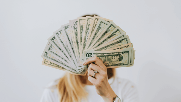 Mujer sosteniendo un abanico de billetes de dólares estadounidenses, ilustrando el concepto de invertir en dólares.