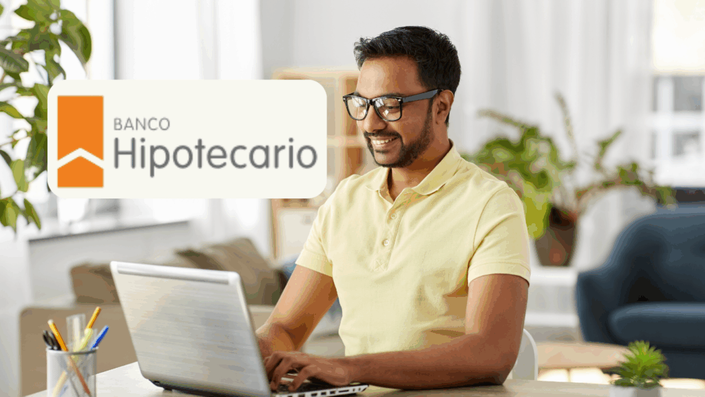 Hombre sonriente usando un laptop mientras trabaja desde su casa, con el logo de Banco Hipotecario visible en la esquina superior izquierda.